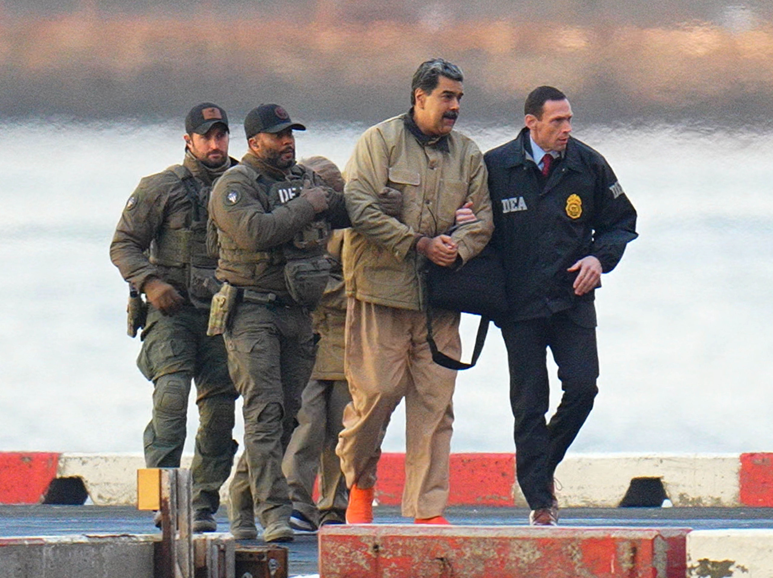 Nicolas Maduro, a tall, slightly heavyset man wearing khakis, is handcuffed and escorted by federal agents