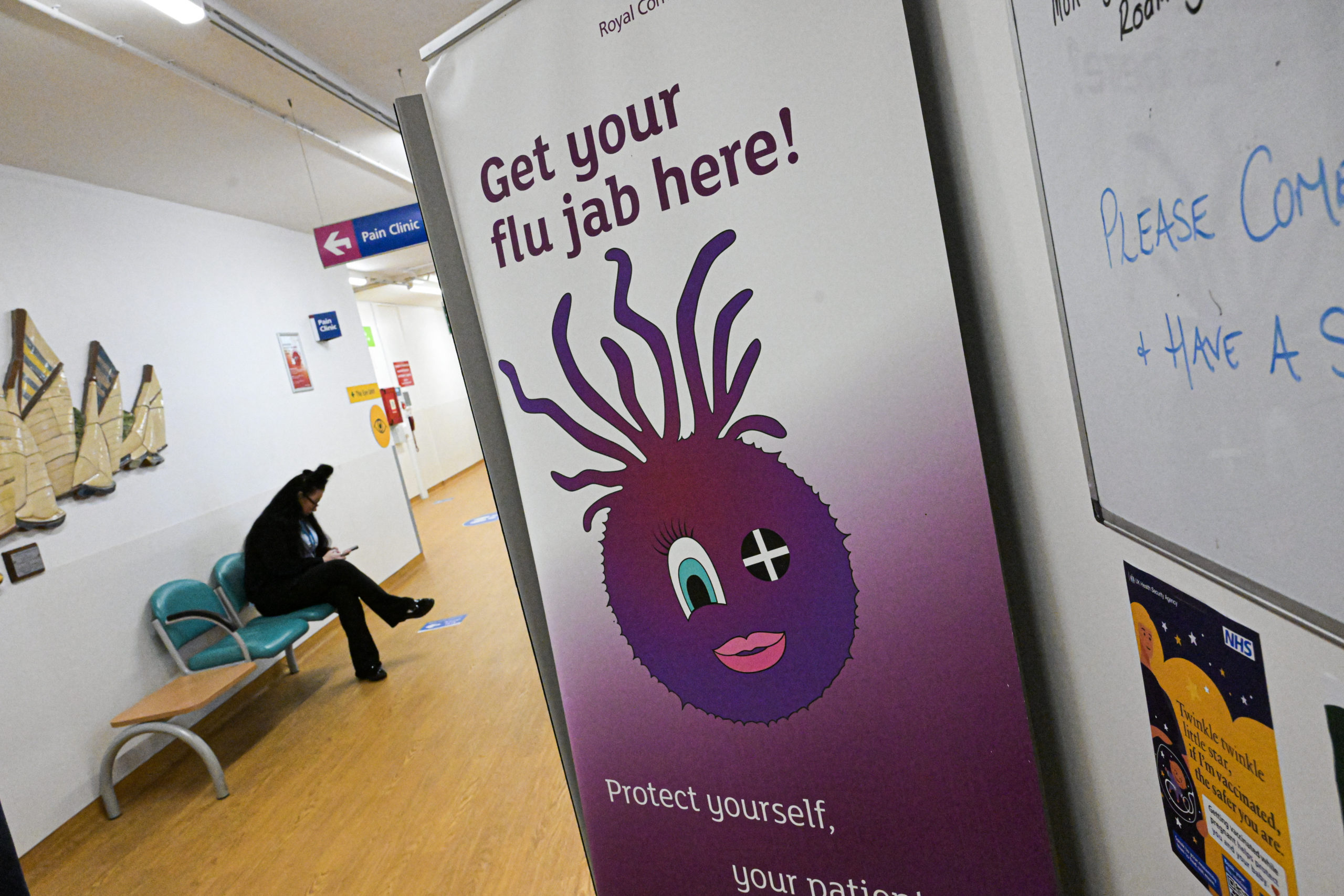 A banner in a hallway featuring a cartoon face reads “Get your flu jab here!”