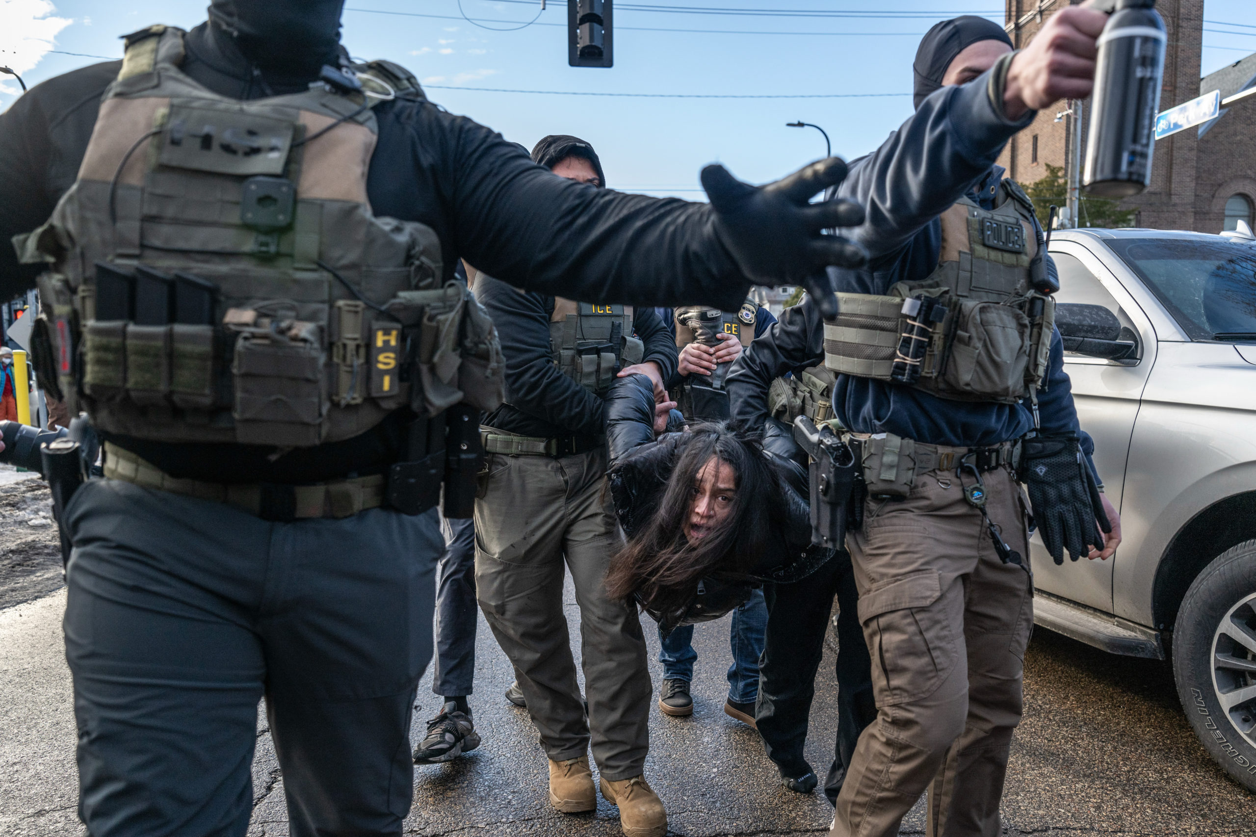 A woman with long dark hair is carried by armed, masked men in tactical vests; one reaches toward the camera.