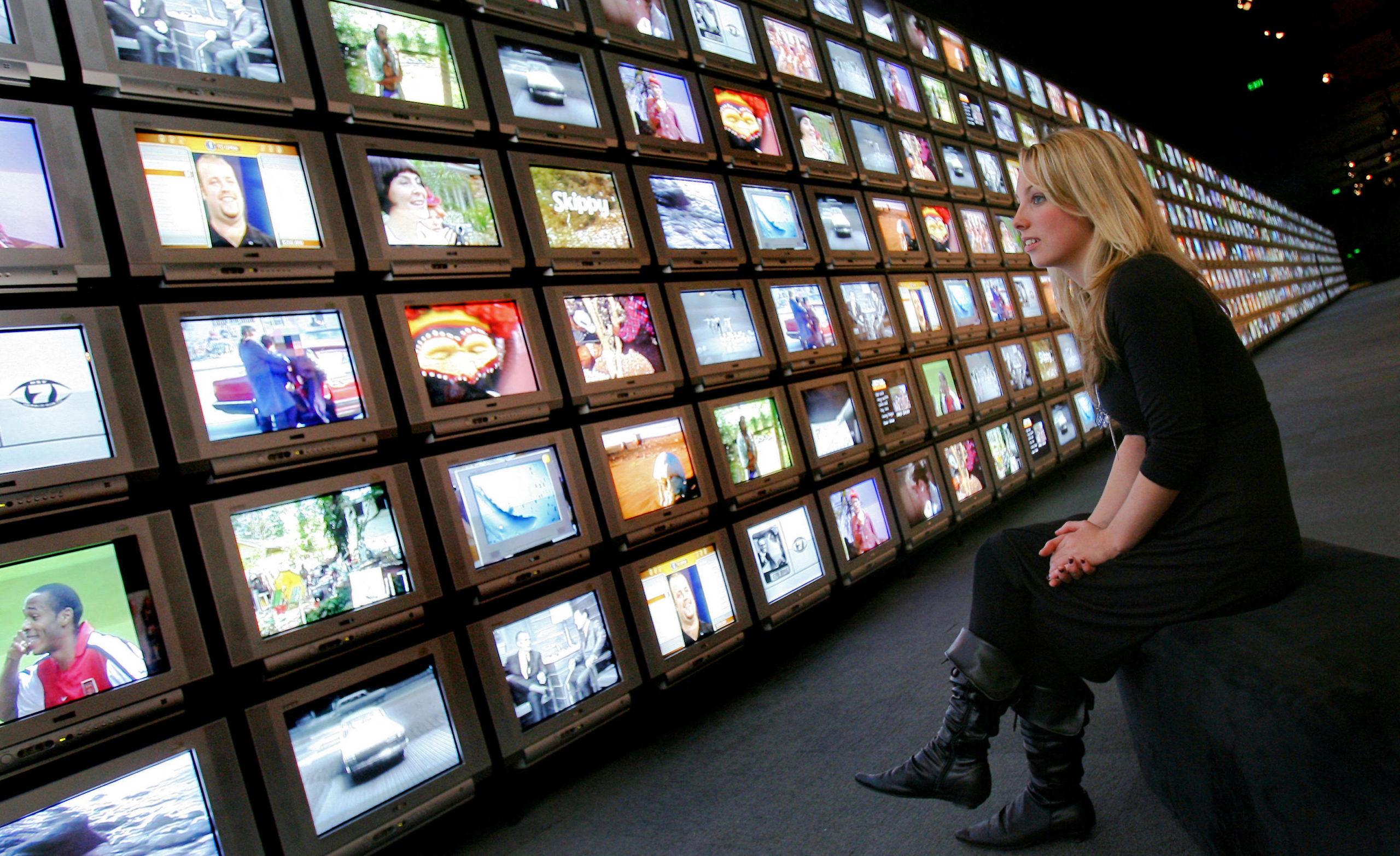 A woman looks at a wall of TV screens.