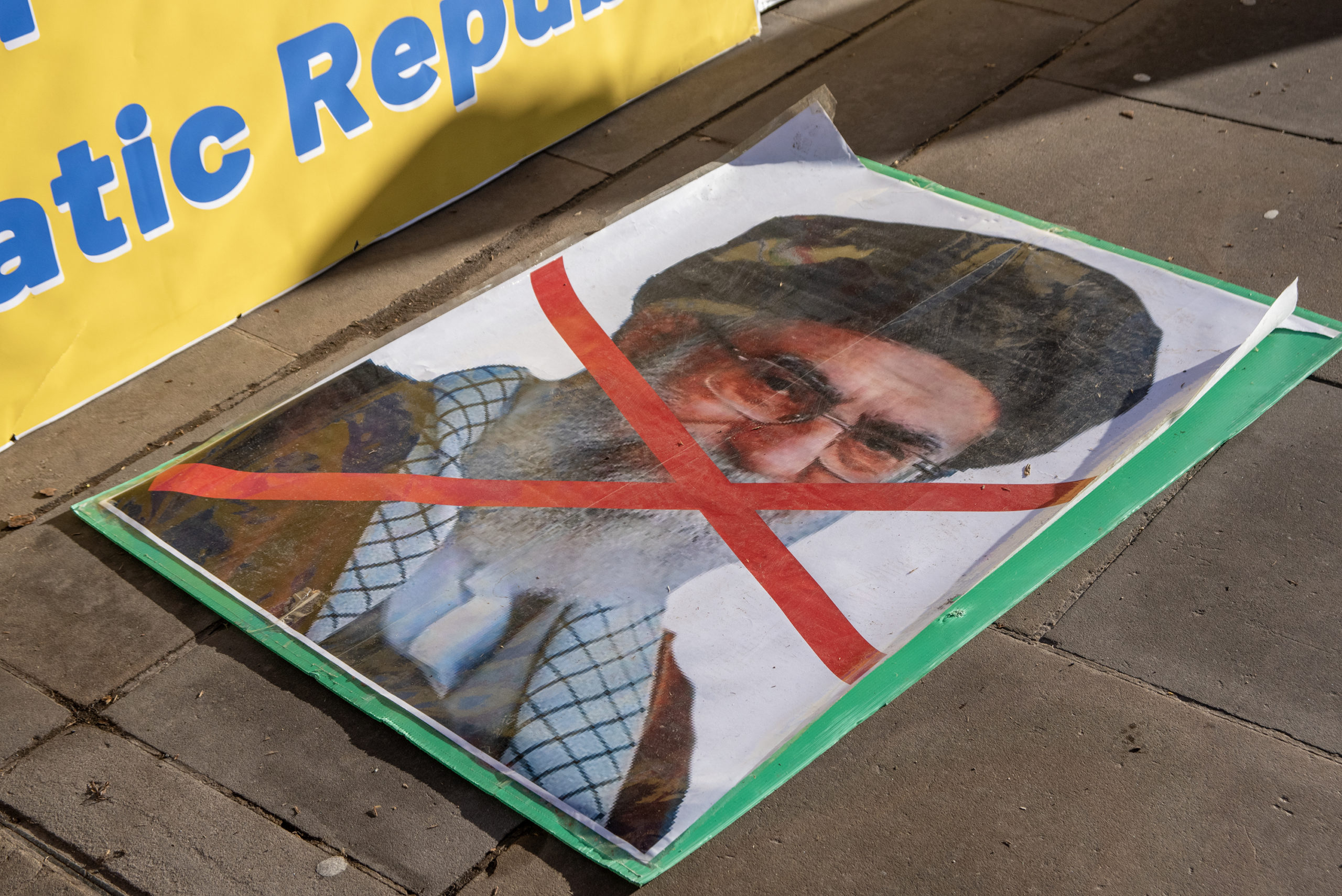 Photo of Khamanei with a red X over his face lying on the sidewalk. 