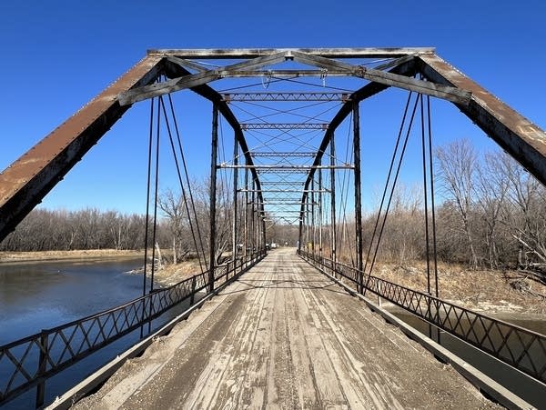 An old metal bridge spans a river in a rural setting