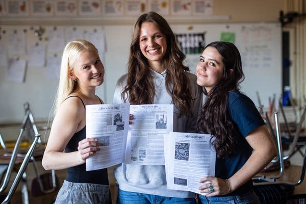 Three students hold up printouts of a newspaper