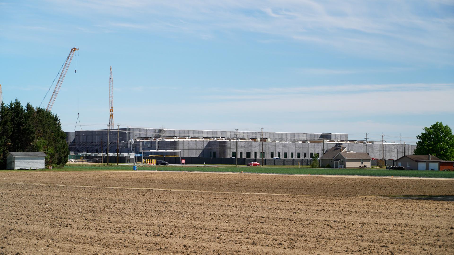 A large data center with gray walls is seen under construction across a field.