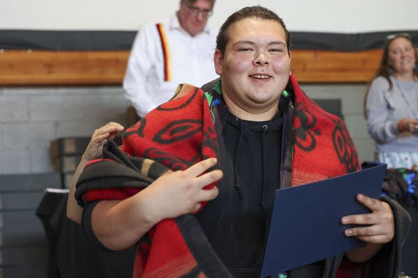 A student holds a red and black blanket over his shoulders.