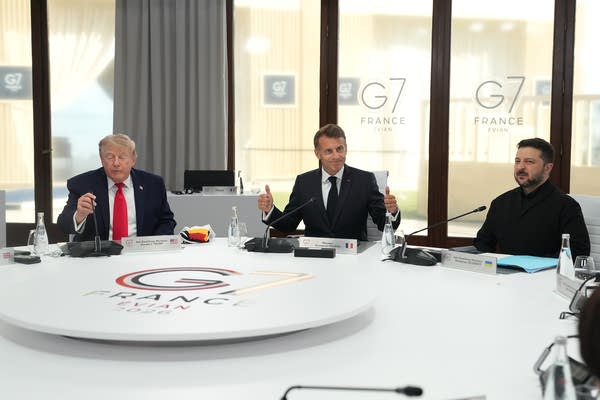 Three world leaders sit at a table while talking.
