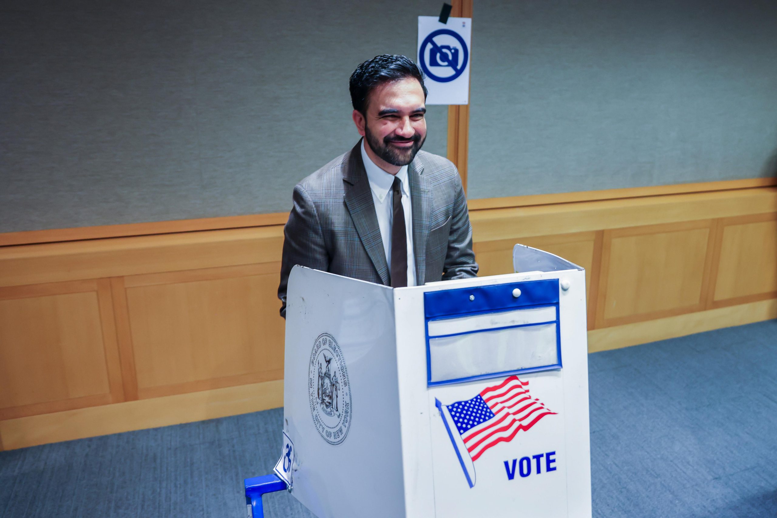 New York Mayor Zohran Mamdani smiles from behind a voting screen.