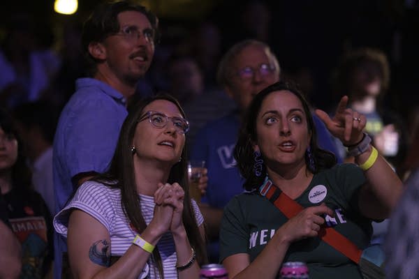 Two women watch election results on a screen.