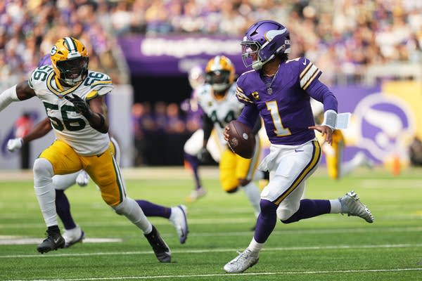 A quarterback runs toward the left of frame holding the ball while facing off against opposing players.