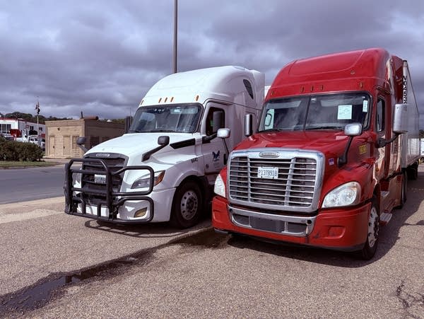 Two semi trucks, white and red, are parked side by side.