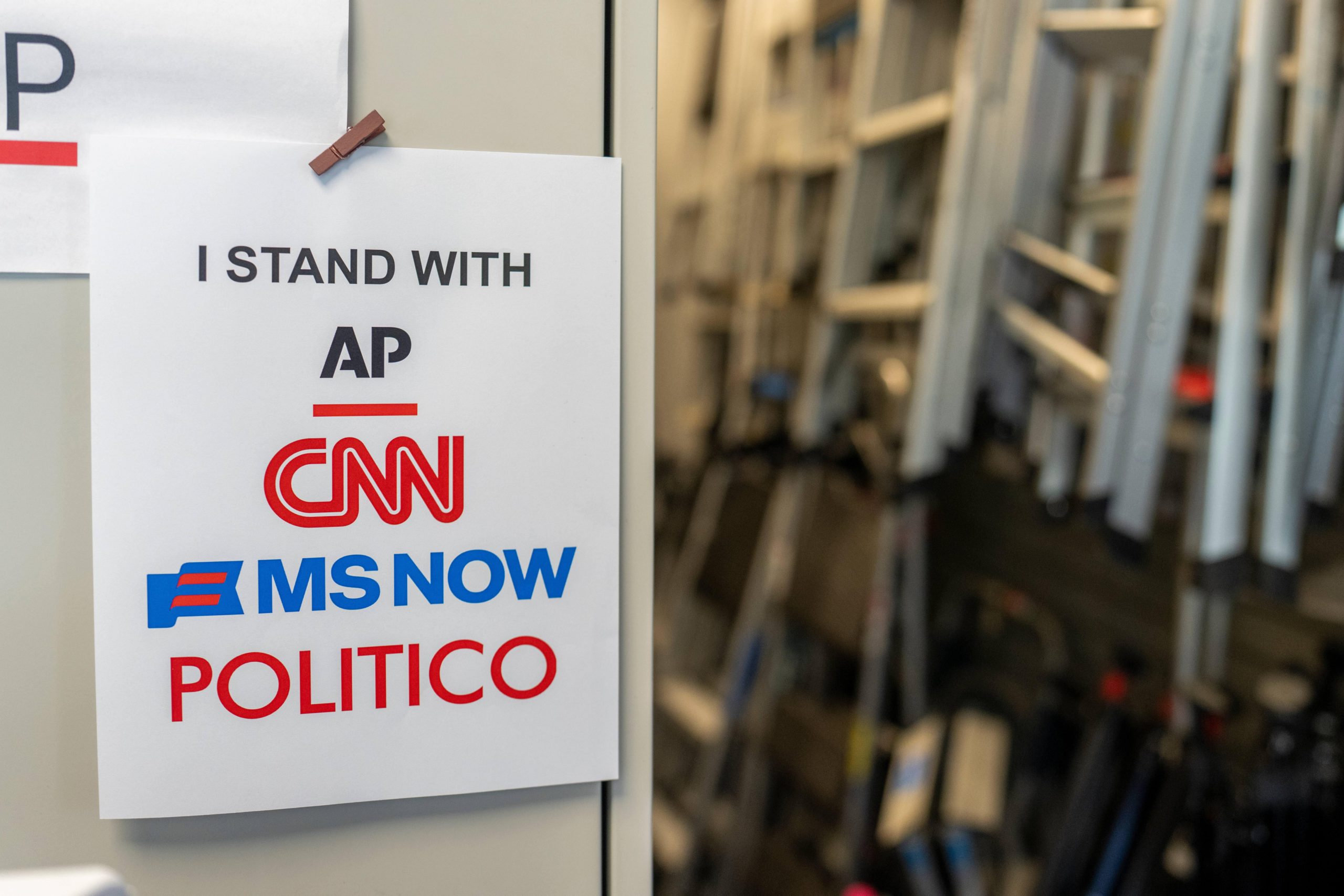 A sign in support of AP, CNN, MS NOW, and Politico hangs near the White House briefing room.