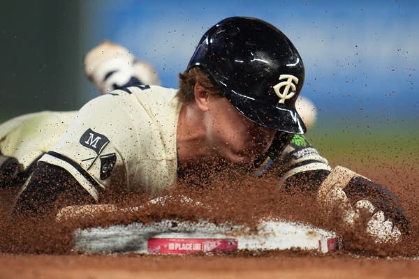 A baseball player kicks up dirt by sliding face-first into a plate.