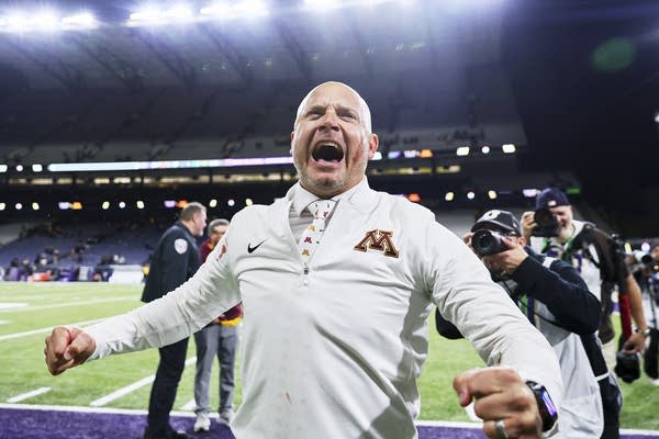 A football coach cheers and pumps his arms with blood smeared on his cheek.