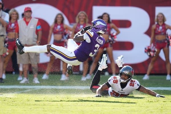 A football player falls backward after catching a ball as an opposing player looks on from a prone position.