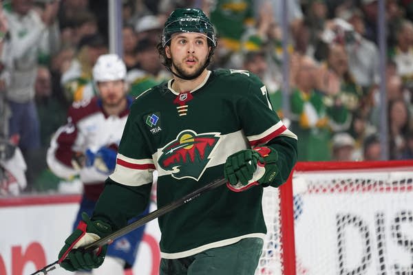 A hockey player in green holds his stick on the ice.