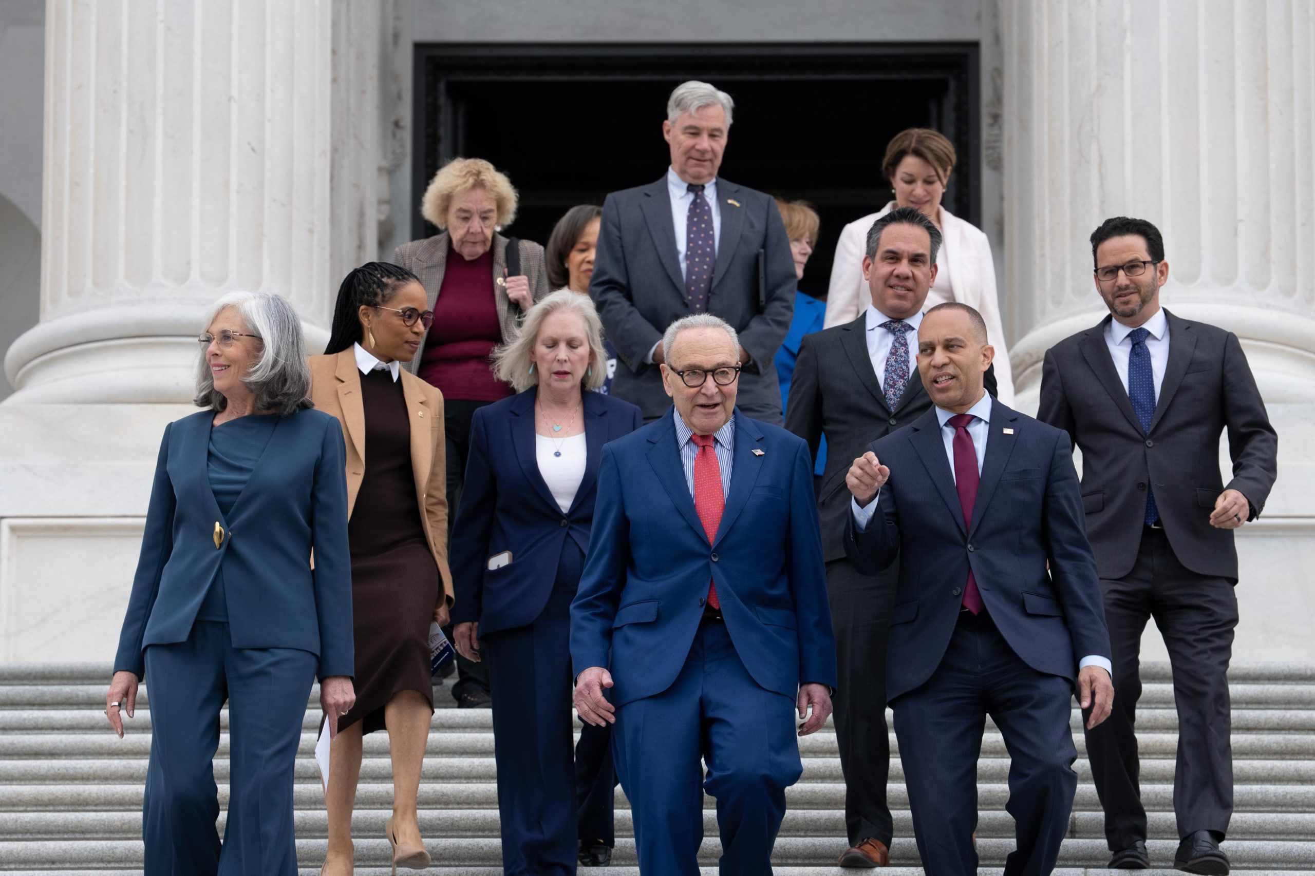 A group of congressional Democrats walk down a flight of stairs outside of the US Capitol, flanked by columns.