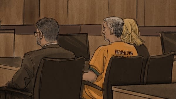 gray haired man in jail uniform sits at defense table