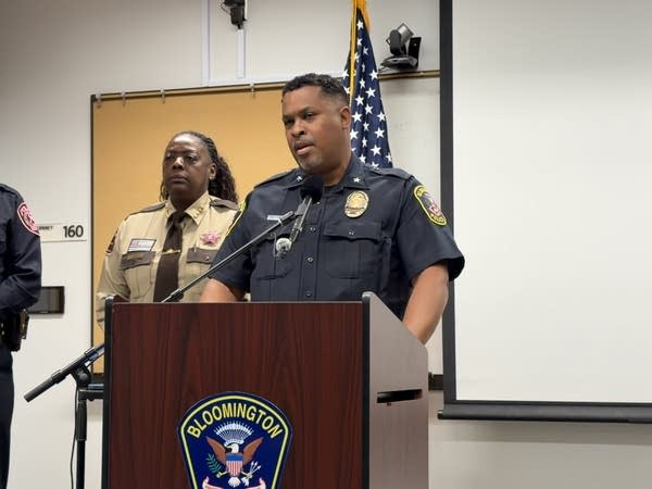 A police officer speaks into a podium in a conference room.