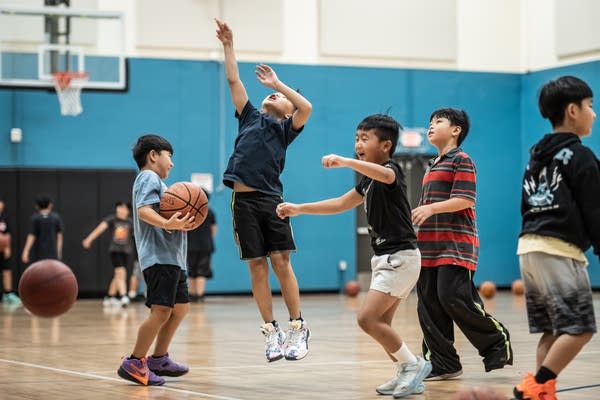 A young boy jumps to shoot a basketball in the middle of a group.