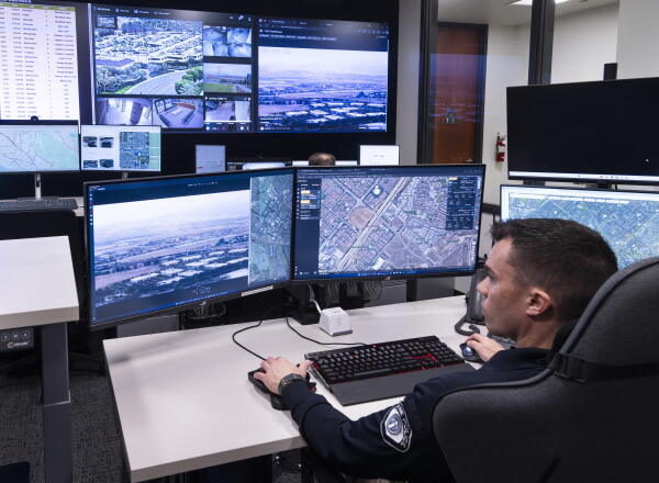 A police officer sits at a desk with multiple computer screens as he monitors video surveillance in the real-time crime center at the Irvine Police Department in California in 2024.
