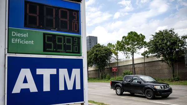 A car drives by prices at a gas station.