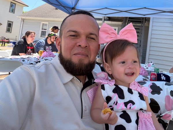 A bearded man in a white shirt poses with his young daughter for a photo.