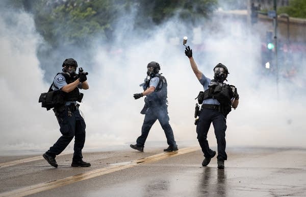 A police officer throws a tear gas canister towards protesters.