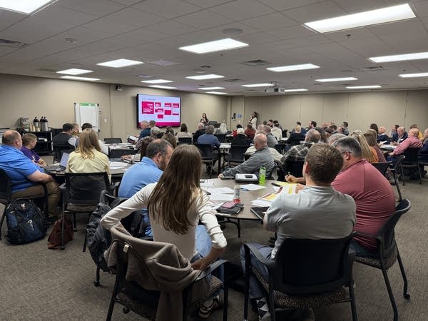 People sit around tables in a workshop inside a large room.
