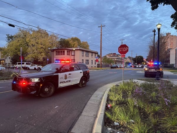Police cars surround a city intersection with their lights on. Police tape blocks off the scene.