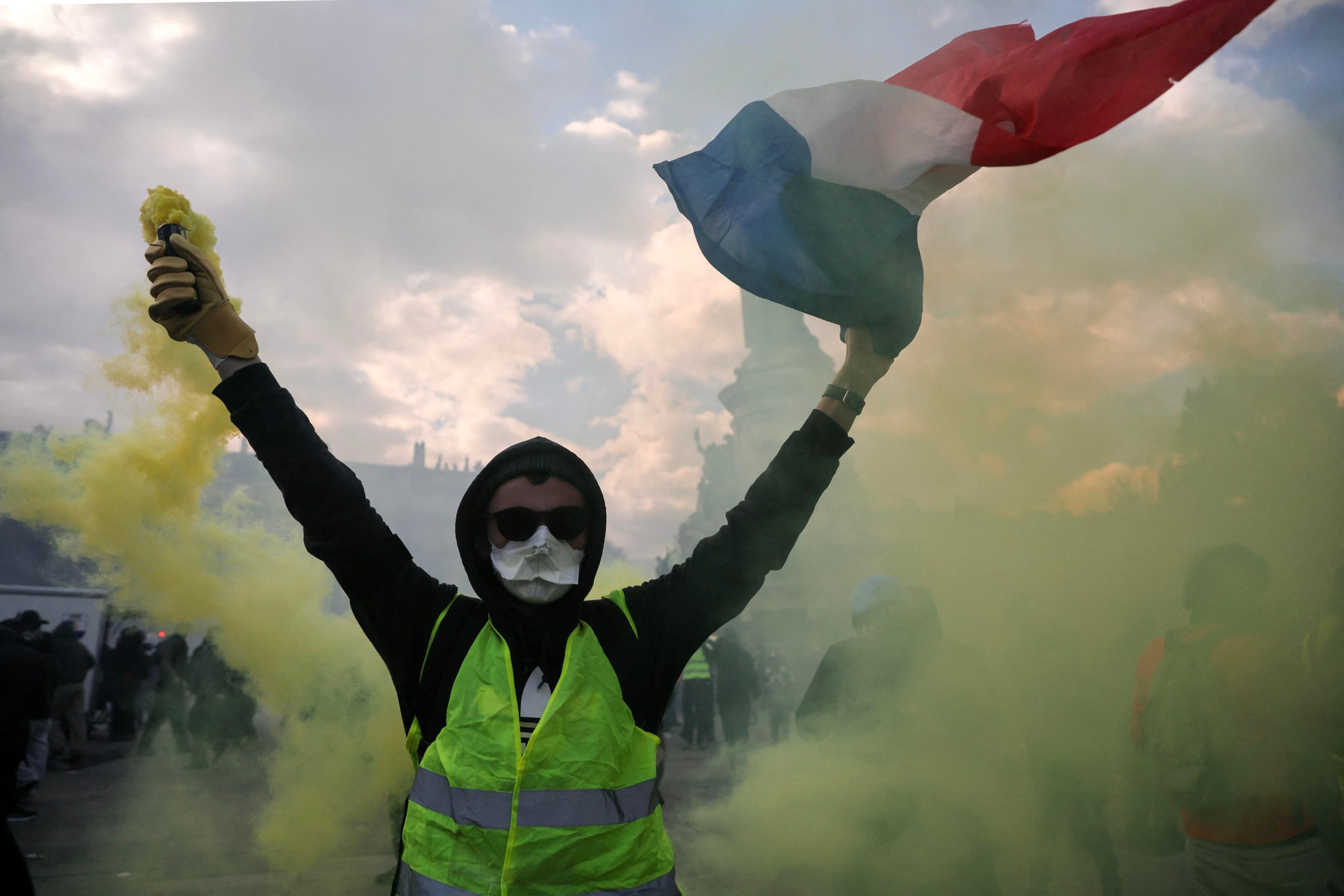 A masked protester holding a smoke flare and French flag