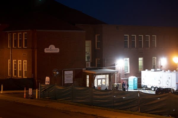A building illuminated on one side with large lighting and a structure in a nearby parking lot.