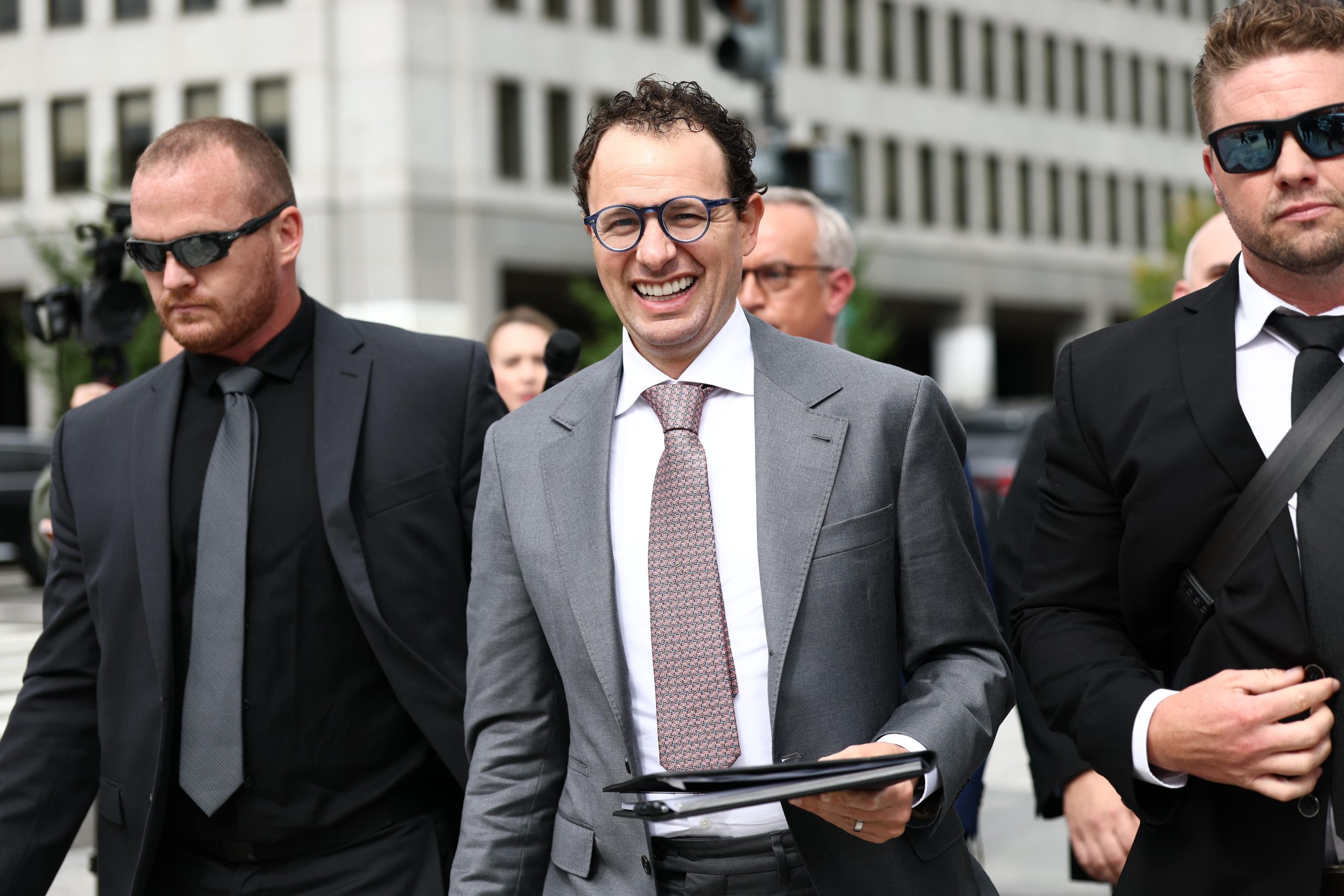 Dario Amodei dressed in a suit walking between bodyguards