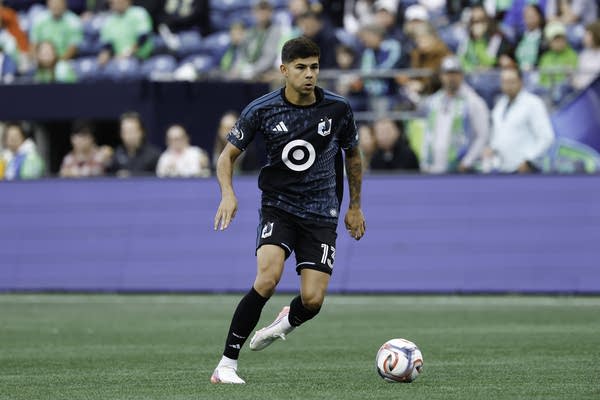 A soccer player in a dark blue uniform runs up to the ball.