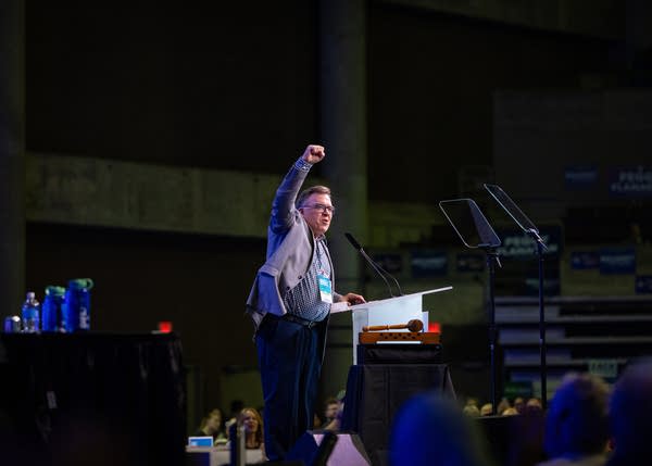 A man speaking on stage raises a fist.