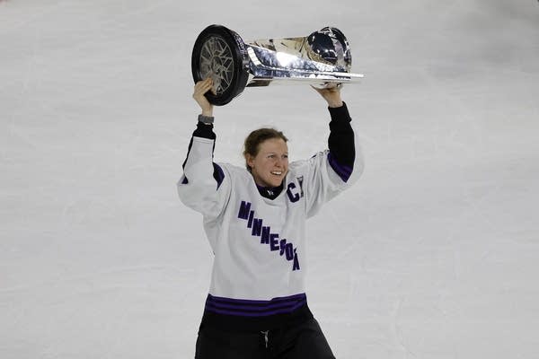 a female hockey player lifts a trophy